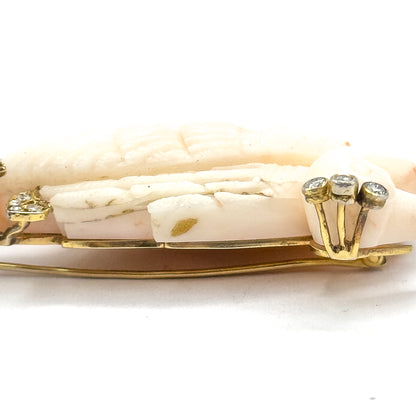 A tight edge-on close-up along the coral's carved feather grooves, with a three-stone diamond cluster raised on prongs at the right and the slim gold pin stem running the full length beneath.