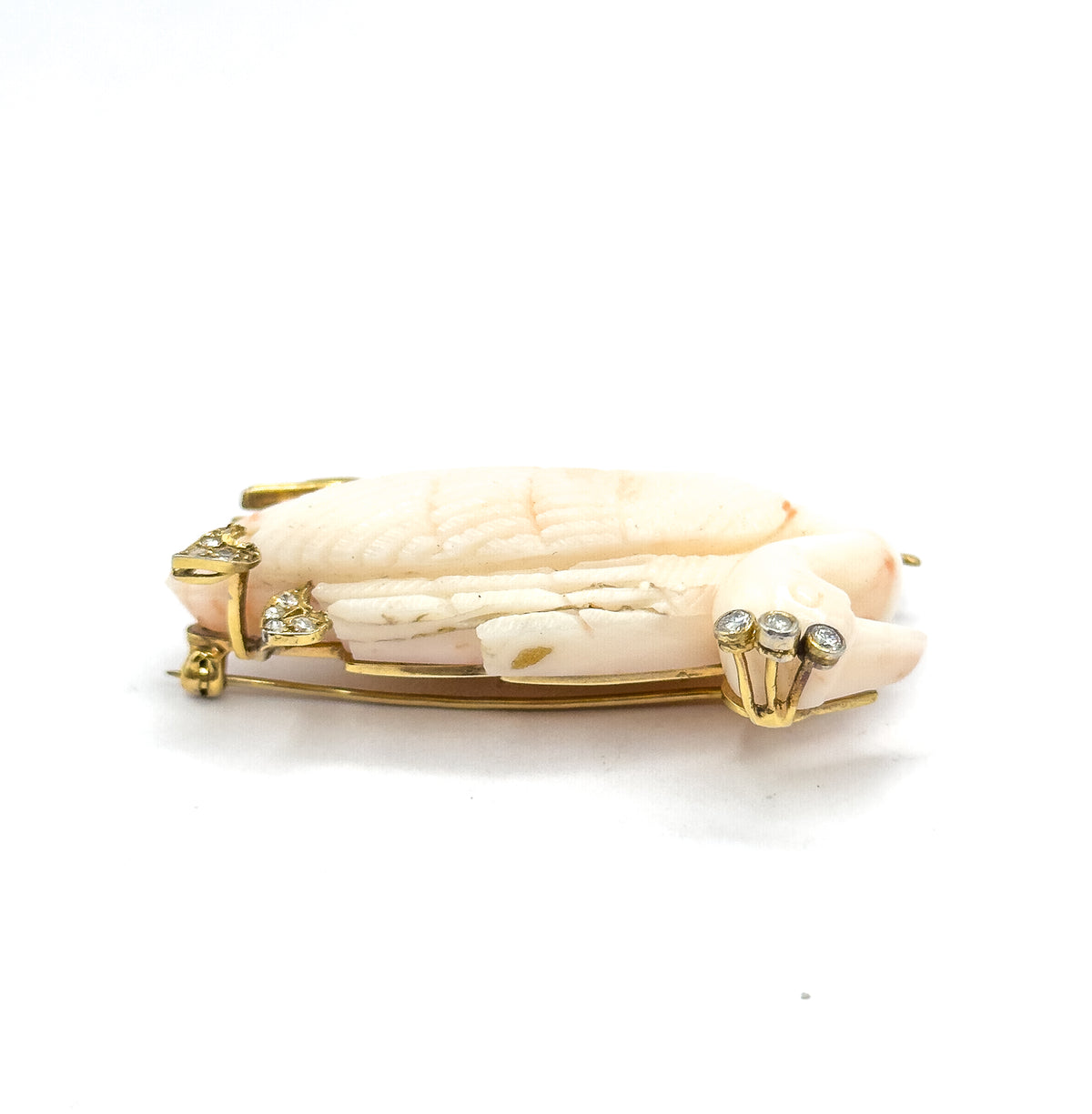A near-level profile from the side, the coral body lying long and low with prong-set diamonds at the head on the right, smaller stones at the left, and the pin stem and catch running below.
