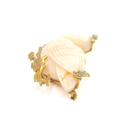 A steep view down onto the carved coral wing, its fine feather ridges filling the frame, with diamond clusters raised on prongs at the upper right and right edge and the textured gold reeds clustered at the left.