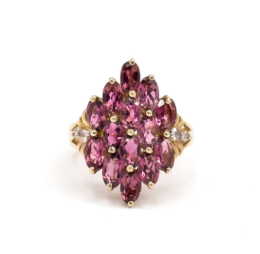 Straight down on the face, the elongated navette cluster of fourteen prong-set oval garnets shows in full symmetry, with a rose cut diamond visible on each yellow gold shoulder.