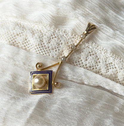 Closer diagonal view showing the three seed pearls spaced along the slender bar and the scrolled gold volutes flanking the cobalt blue enamel square, with the creamy pearl in its milgrain setting.