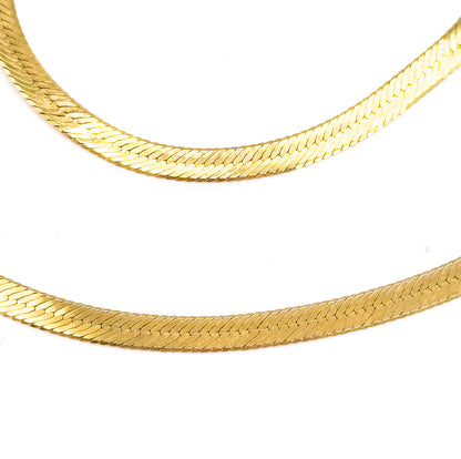 Two sweeping curves of the herringbone chain fill the frame in close macro on white, the flat 10 karat yellow gold weave showing its fine angled links.