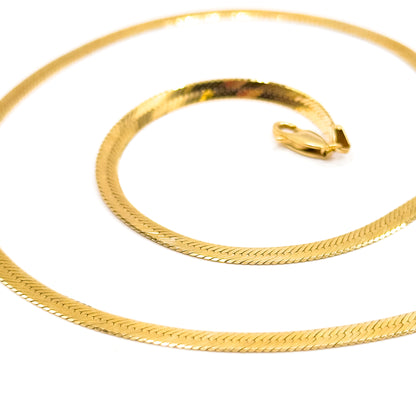 The chain coiled in a flat spiral on white, each loop nesting inside the last, with the lobster clasp and its ring fitting resting together at the centre.