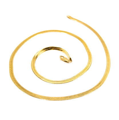 The full chain spiralled wide across white with one flat tapered end lifting free at the upper right, while the lobster clasp sits alone at the centre of the coil.