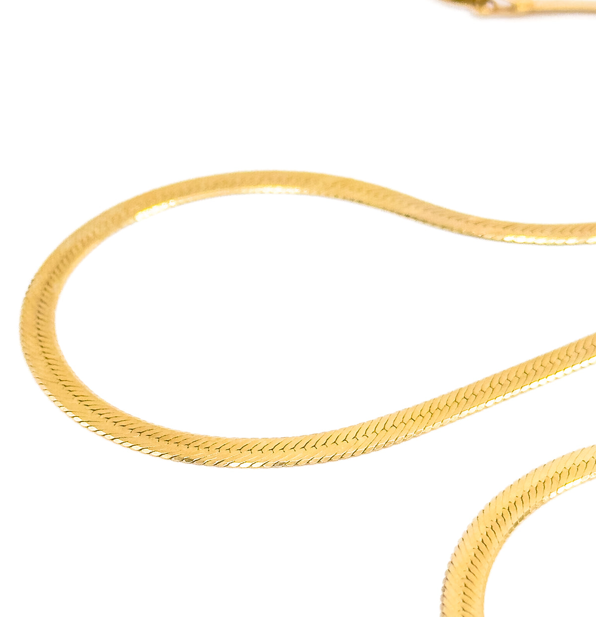 Close macro on white, the chain laid in loose S-curves so the flat herringbone weave and its fine diagonal ridges fill the frame, with part of the clasp blurred at top.