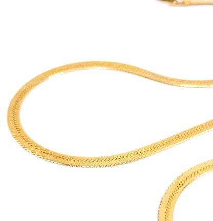 Close macro on white, the chain laid in loose S-curves so the flat herringbone weave and its fine diagonal ridges fill the frame, with part of the clasp blurred at top.