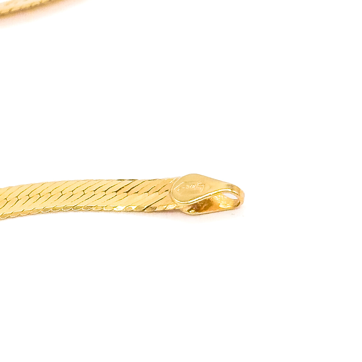 The chain's end fitting in sharp macro on white, a rounded flat tag with a small stamped mark meeting the herringbone weave at the clasp end.