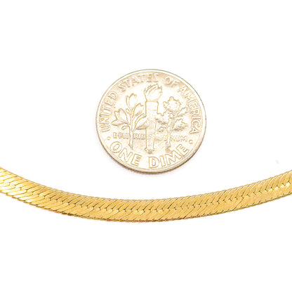 A gently curving length of the 10 karat yellow gold herringbone chain beneath a US dime on white, the coin giving a clear sense of the flat weave's narrow width.
