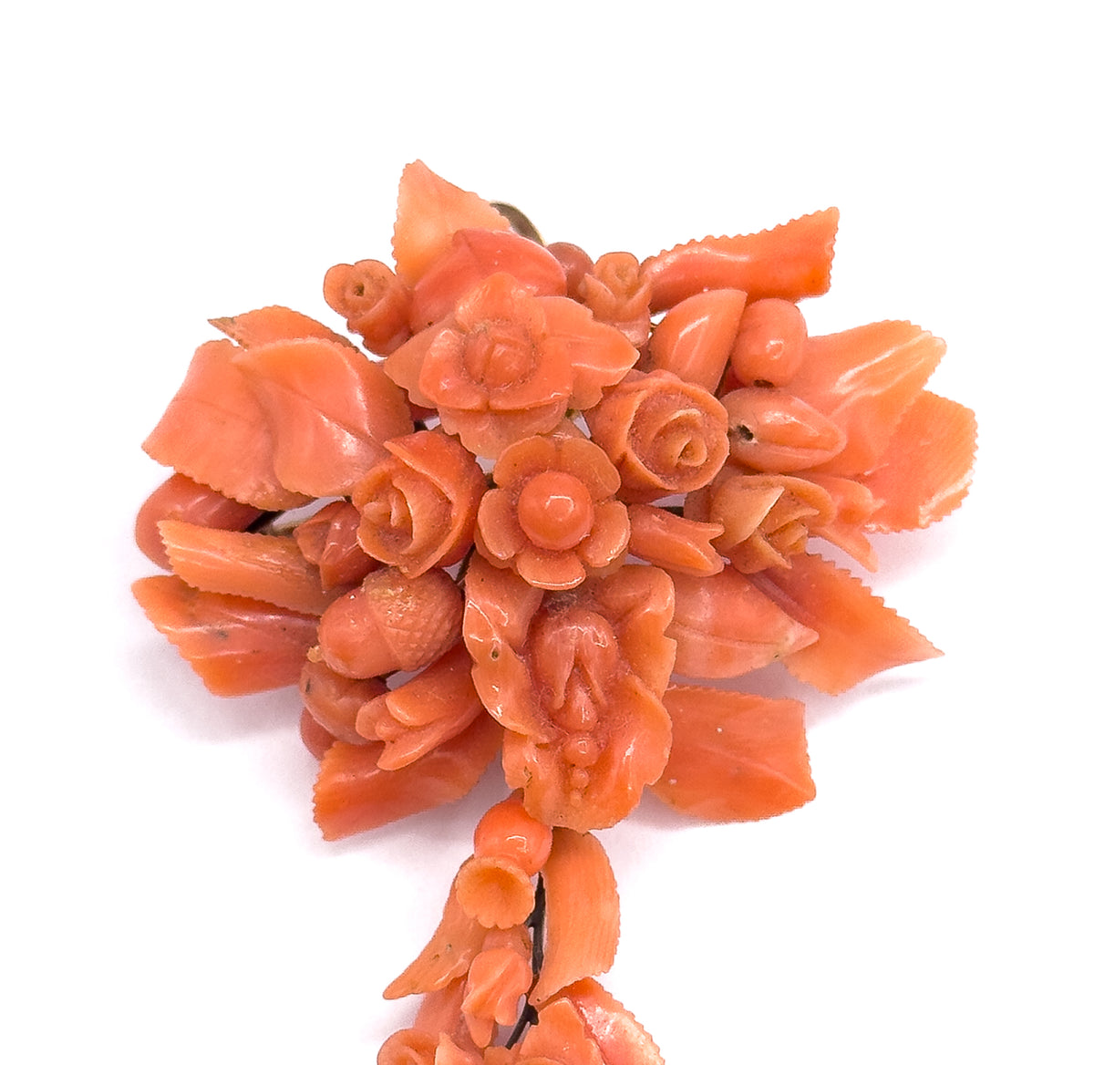 A close view of the upper cluster, where carved salmon pink coral roses, open flowers, buds and serrated leaves overlap in deep layers above the narrowing tail.