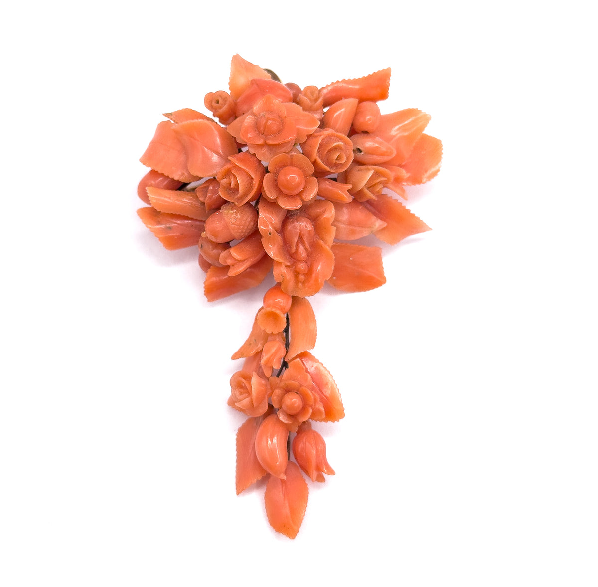 The whole pendant brooch face up against plain white, its broad upper cluster of carved salmon pink coral flowers and leaves tapering into a slender hanging tail of buds and foliage.