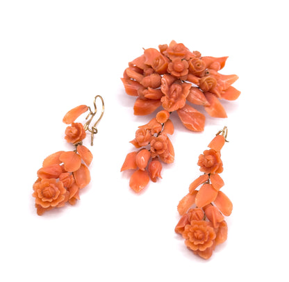 The complete set laid out together, the pendant brooch above and both carved coral drop earrings angled below, their yellow gold hook fittings curving at the tops.