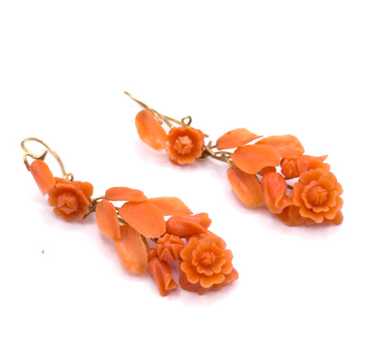 A low three-quarter view along the pair, the salmon pink coral roses and leaves rising toward the camera while the slender yellow gold hook wires curve away behind.