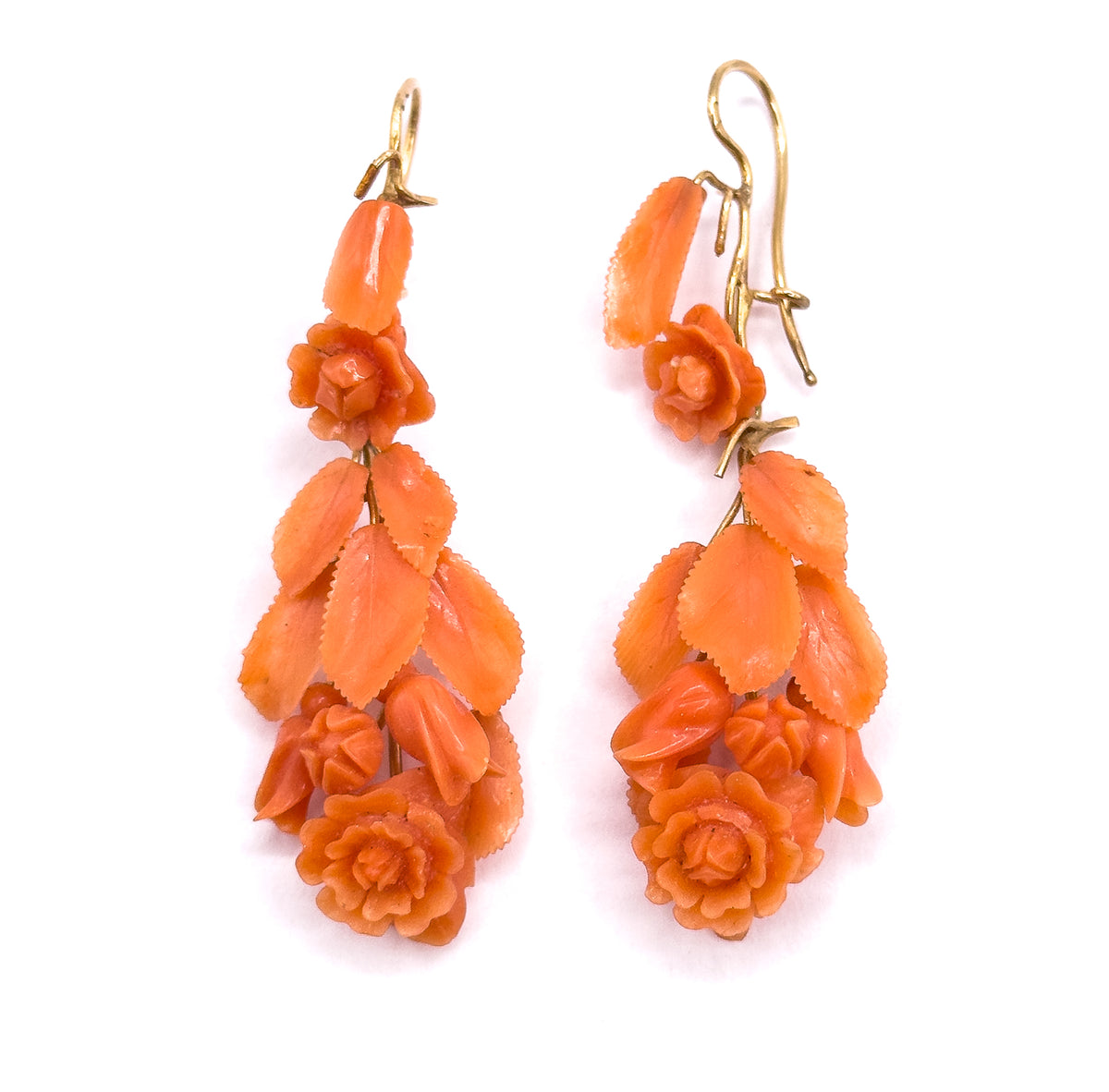 Both earrings stand upright side by side, the yellow gold hook wires crossing at the top above long tapering cascades of carved coral leaves ending in full open roses.