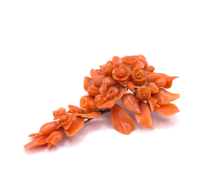The whole carved coral cluster laid flat on its side and seen in full length, the spray of roses, buds and serrated leaves tapering diagonally away with the slim yellow gold stem wire running beneath.