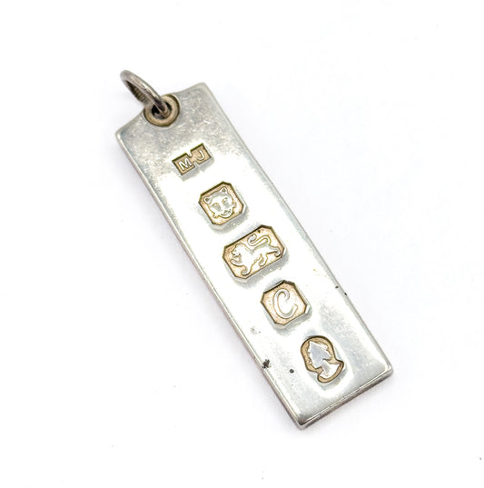 A close view down the pendant's hallmarked face, where five raised stamped marks — letters, two animal figures and a profile head — run in a line beneath the round bail.