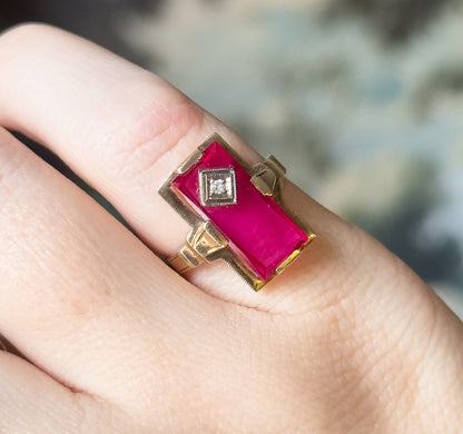 Close view from above the finger, the red stone's deep pink-red surface catching light and the stepped yellow gold shoulders flanking the face coming into focus.