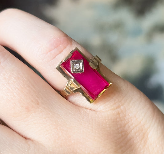Close view from above the finger, the red stone's deep pink-red surface catching light and the stepped yellow gold shoulders flanking the face coming into focus.