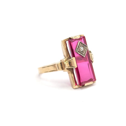 Side-on profile against white, revealing how high the long red stone sits above the finger on its yellow gold gallery, with the diamond's milgrain bezel seen edgewise.