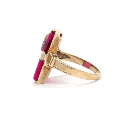 Viewed edge-on from the opposite side, the narrow rim of the elongated face stands upright with the red stone just visible along its edge and the yellow gold shank curving away in a full loop.