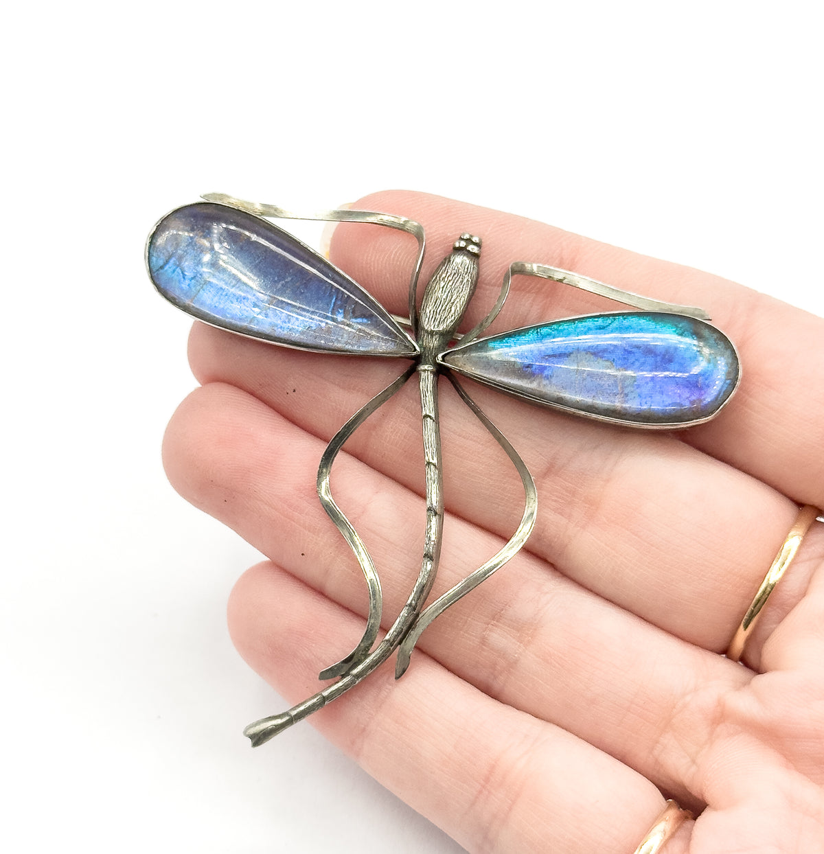 A sterling silver and base metal dragonfly brooch with blue and purple iridescent Morpho butterfly wings under clear domes, shown resting on an open palm for scale.