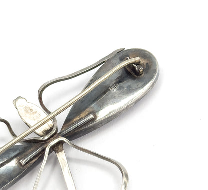 The reverse of the brooch, close in on the tail end, showing the long pin stem across the body, the hinged catch and small maker's marks struck into the darker patina.