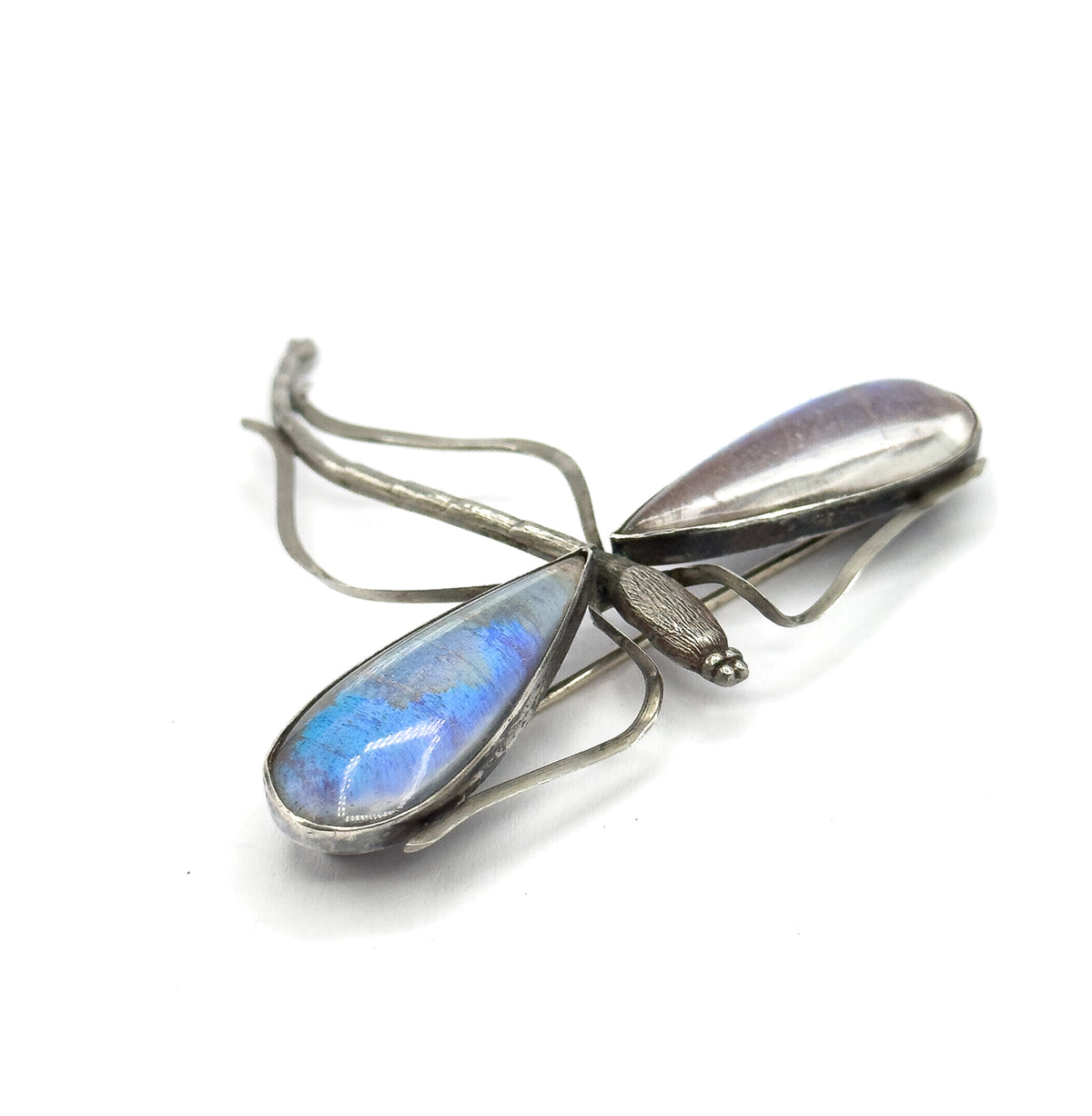 Tipped so one domed wing glows bright blue while the other reads pale silvery, with the textured body, tiny beaded head and the pin stem showing through the open wire frames behind.