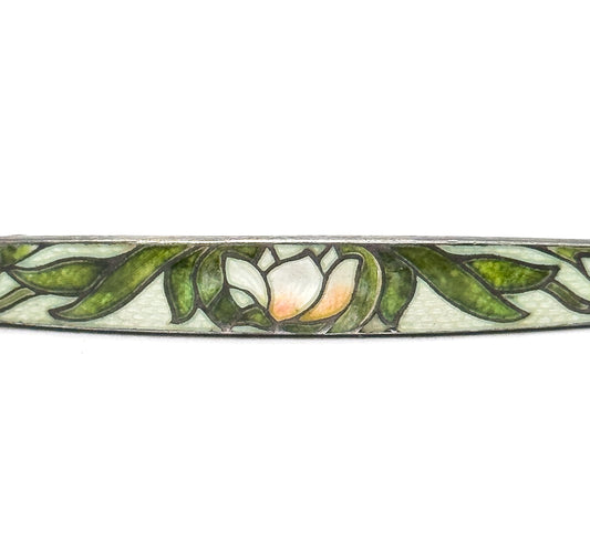 Close crop on the centre of the bar, where a single white blossom with a peach-toned heart sits among green leaves, each shape outlined by fine cloisonné wires on the pale textured ground.