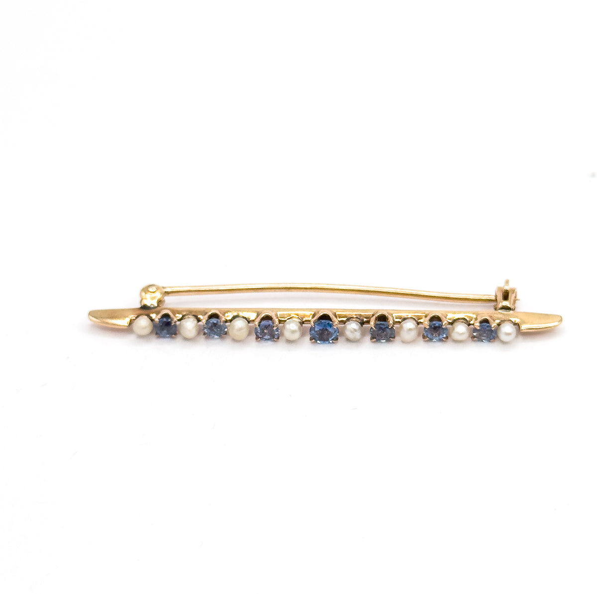 Full-length side view against white with the pin stem swung open and arching above the bar, hinge at the left and catch at the right, the sapphires and seed pearls in a level row below.