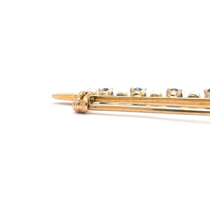 Close view of one end of the bar, showing the pointed pin stem and the yellow gold hinge joint beneath the first prong-set sapphires and seed pearls.