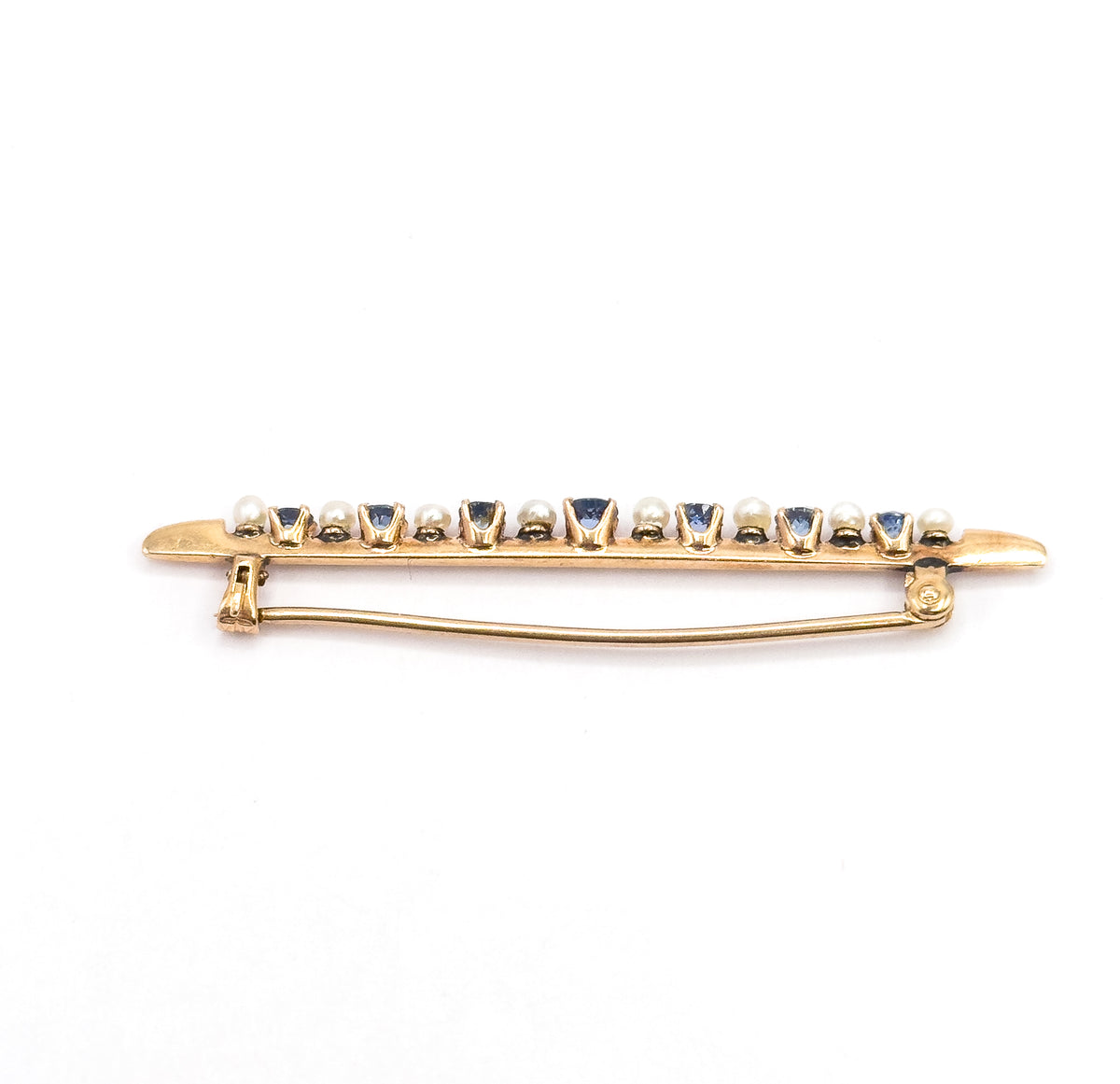 Edge-on view of the whole brooch from behind, the pin stem swept across the back between hinge and catch, with the row of sapphires and seed pearls seen in profile above.
