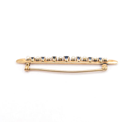Edge-on view of the whole brooch from behind, the pin stem swept across the back between hinge and catch, with the row of sapphires and seed pearls seen in profile above.