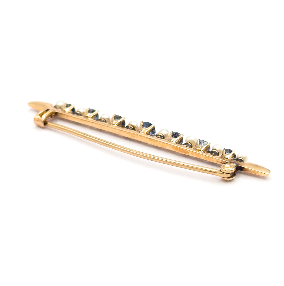 Angled three-quarter view from the back and below, the pin stem bowed across the length of the bar, so the alternating sapphires and seed pearls rise in a sparkling line above it.