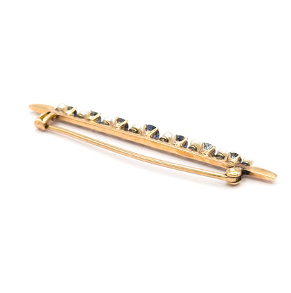 Angled three-quarter view from the back and below, the pin stem bowed across the length of the bar, so the alternating sapphires and seed pearls rise in a sparkling line above it.