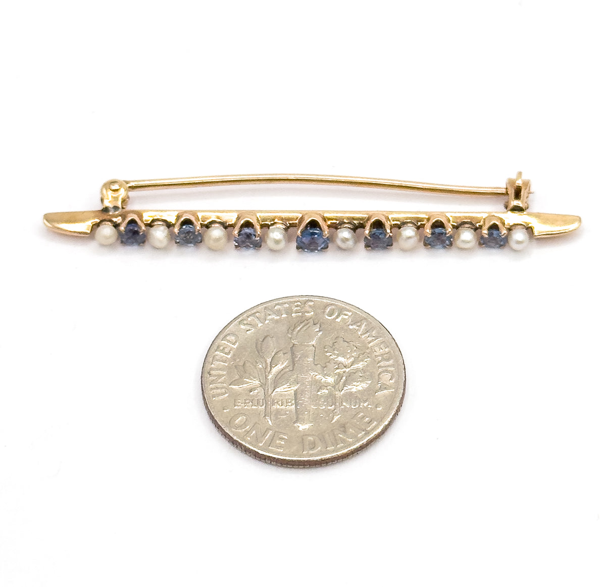 The whole brooch lying above a ten-cent coin for scale, its alternating sapphires and seed pearls spanning a little under twice the coin's width.