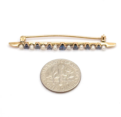 The whole brooch lying above a ten-cent coin for scale, its alternating sapphires and seed pearls spanning a little under twice the coin's width.