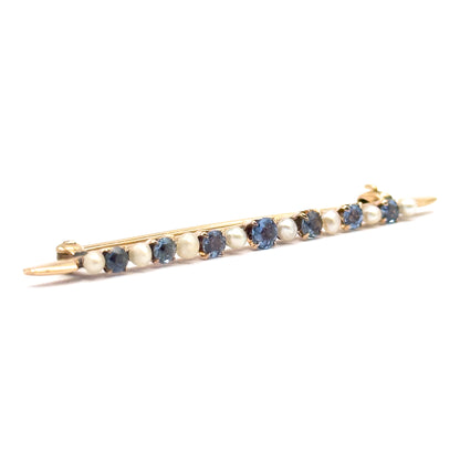 Diagonal view from the front with the bar angled across the frame, the alternating sapphires and seed pearls facing the viewer and the pin stem tips and catch showing at either end.