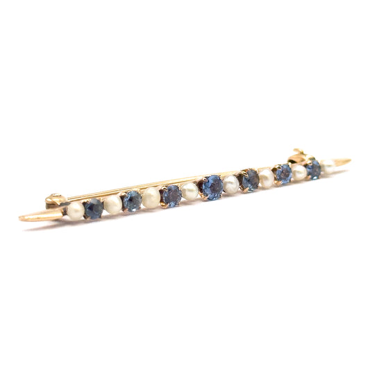 Diagonal view from the front with the bar angled across the frame, the alternating sapphires and seed pearls facing the viewer and the pin stem tips and catch showing at either end.