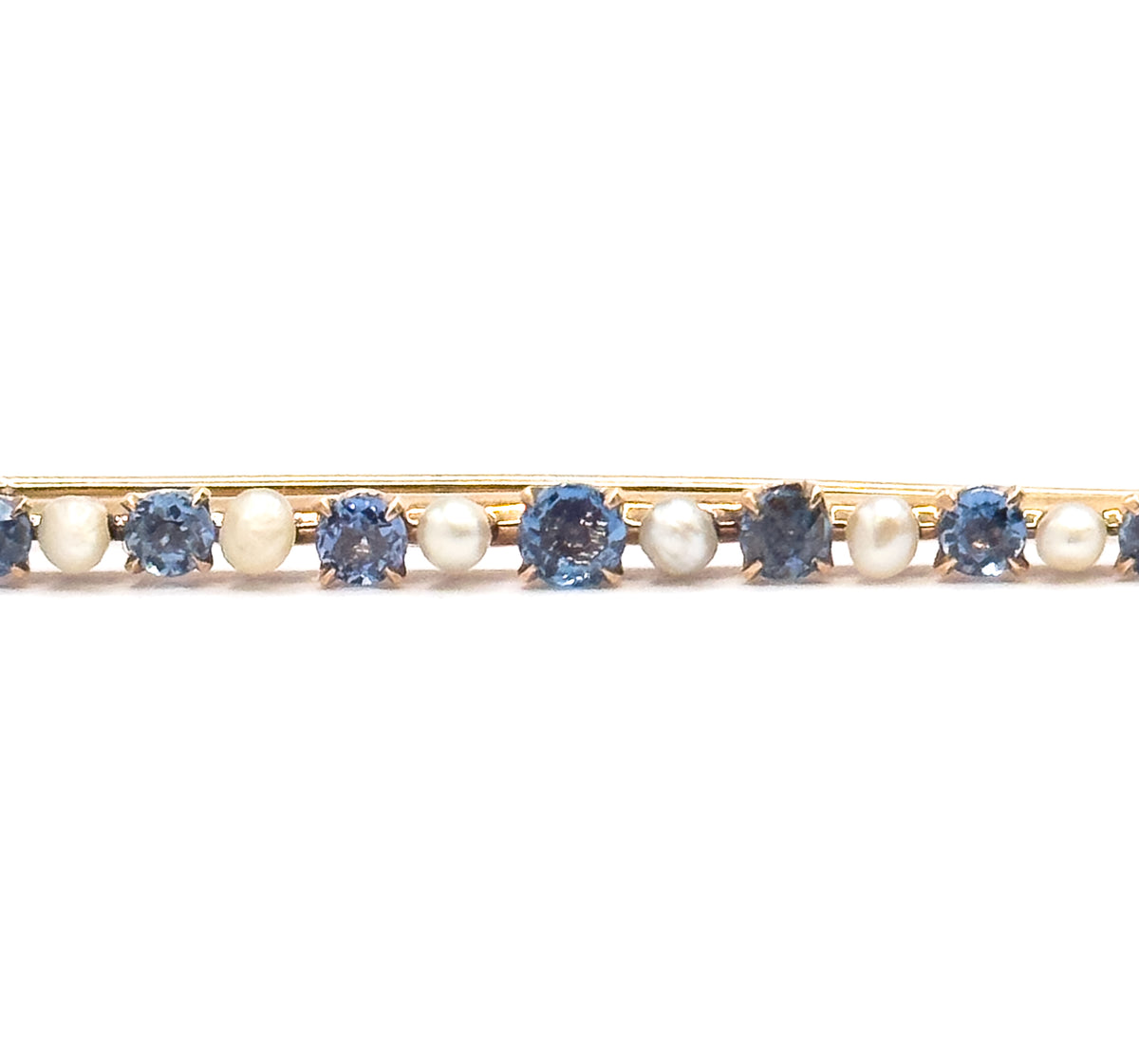 Close crop on the centre of the bar, filling the frame with the largest cornflower sapphire and its prongs flanked by creamy seed pearls and smaller stones either side.