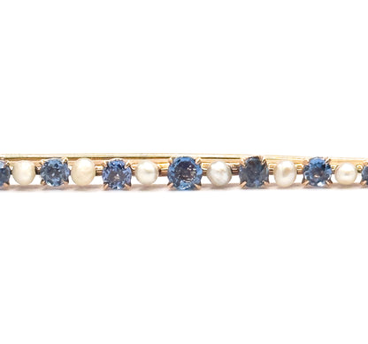 Close crop on the centre of the bar, filling the frame with the largest cornflower sapphire and its prongs flanked by creamy seed pearls and smaller stones either side.