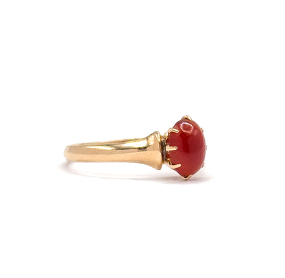 Side profile off the hand, showing the oval orange cabochon gripped by slender prongs and the shank flaring up into the shoulder before meeting the setting.