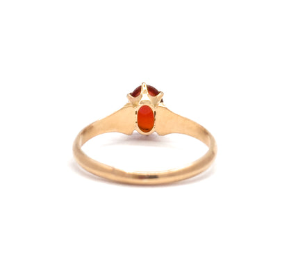 Viewed from behind, the open back of the setting reveals the underside of the oval orange cabochon between the prongs, with the slim yellow gold shank curving below.