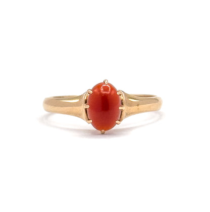 Close front view of the ring face standing upright, the oval orange cabochon held by six slender prongs with the polished yellow gold shoulders flaring out to the shank on each side.