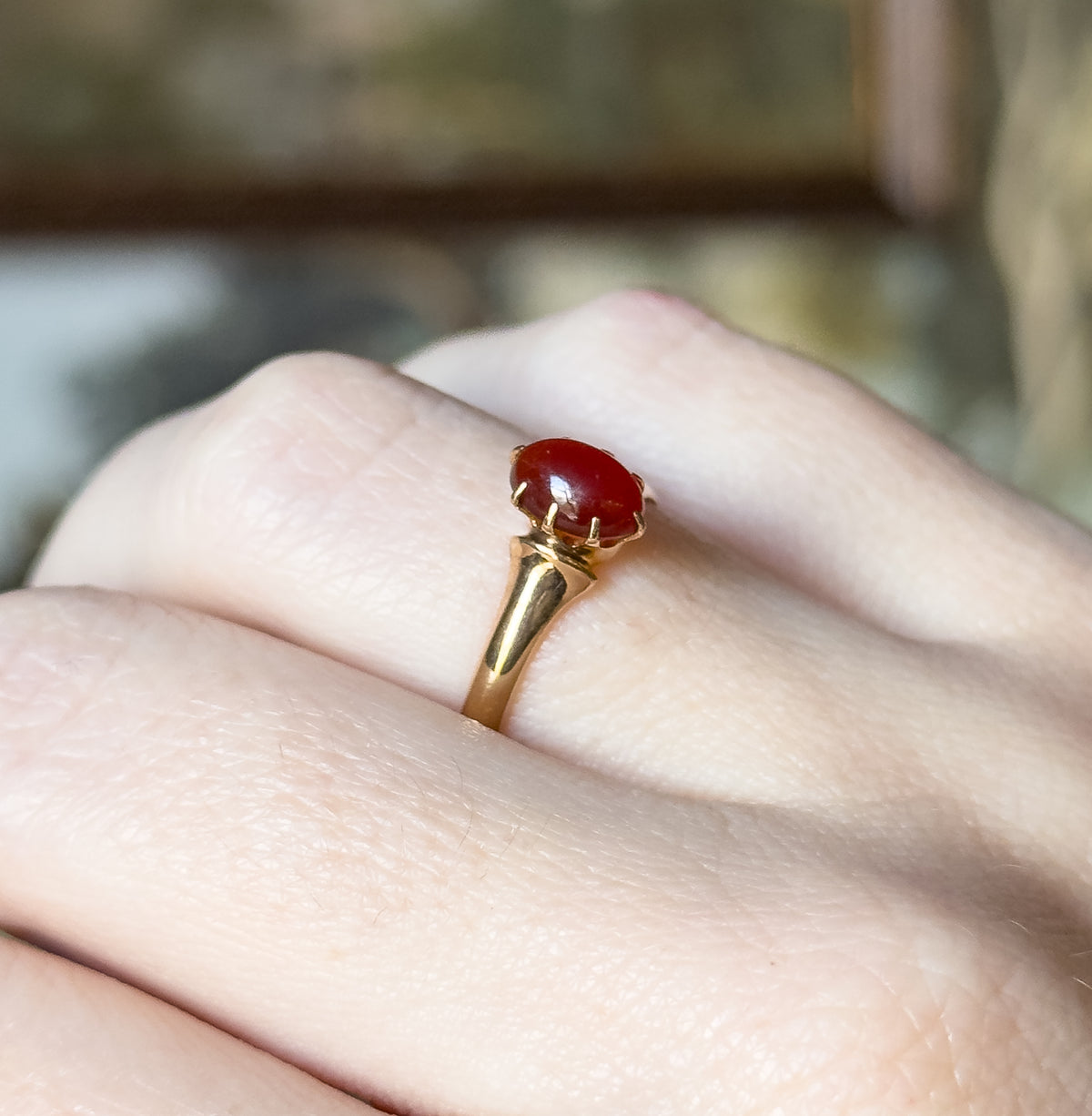 Art Deco oval orange glass cabochon ring in 10K yellow gold, shown on a finger, the claw-held stone raised above a smooth shank that tapers as it meets the setting.