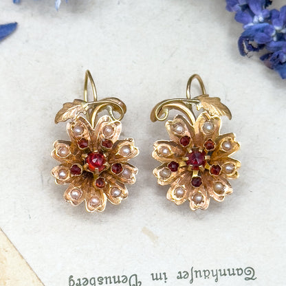 Pair of gold floral earrings with red and pearl accents on a white surface with blue flowers.