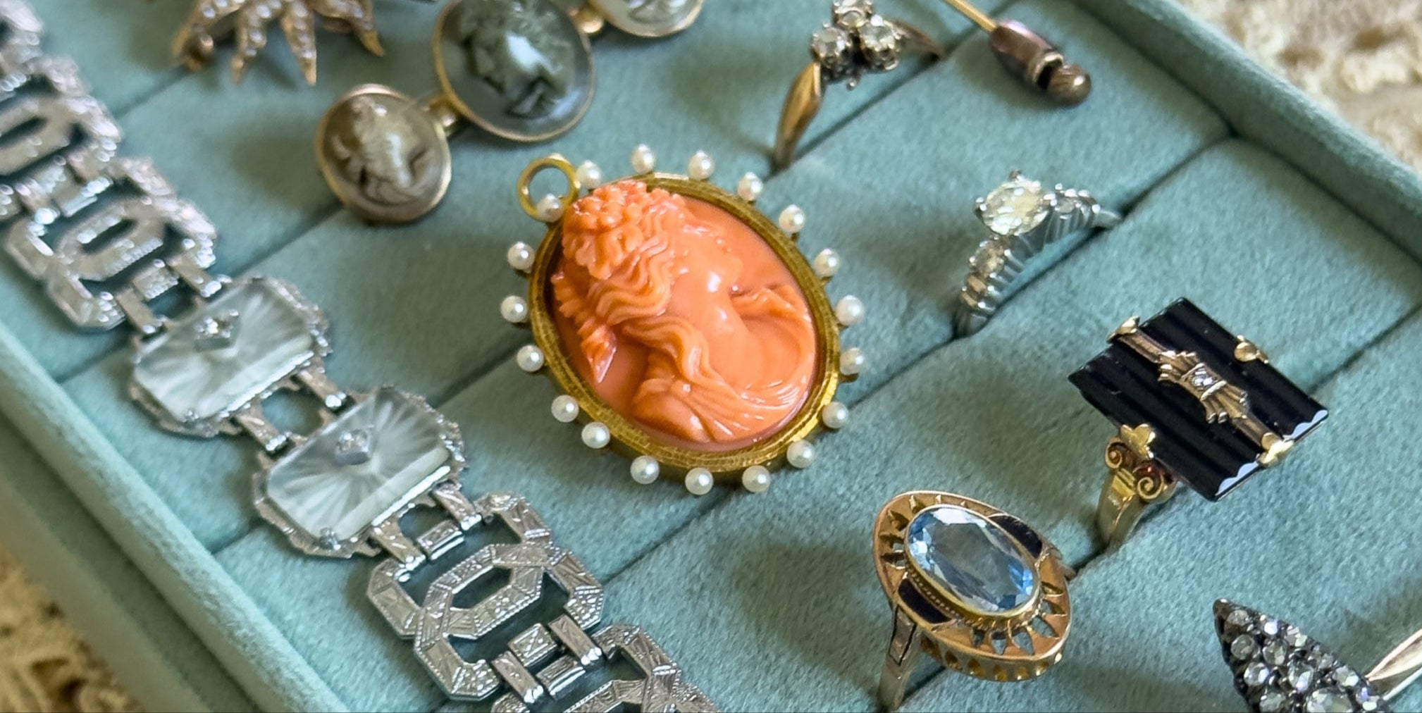 Collection of vintage jewelry including rings, brooches, and a bracelet on a turquoise jewelry box.