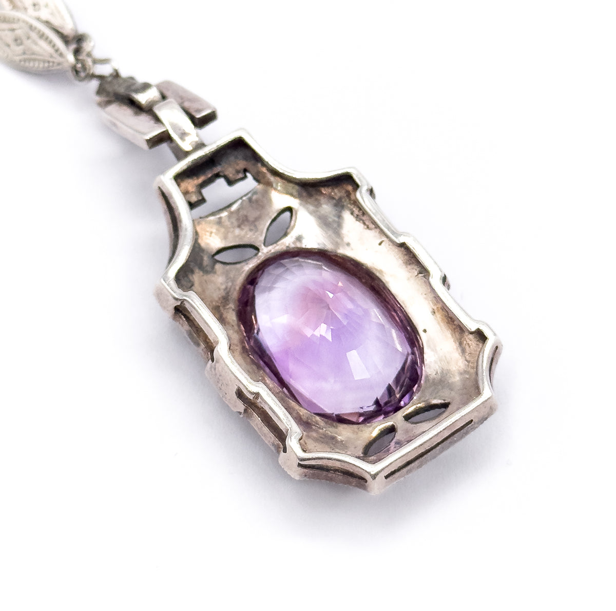 The back of a single necklace drop, its shield-shaped silver plate pierced with leaf-shaped cut-outs around the open bezel, with the amethyst pavilion visible and articulated links above.