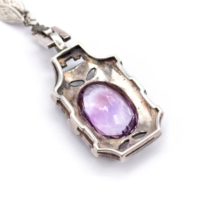 The back of a single necklace drop, its shield-shaped silver plate pierced with leaf-shaped cut-outs around the open bezel, with the amethyst pavilion visible and articulated links above.