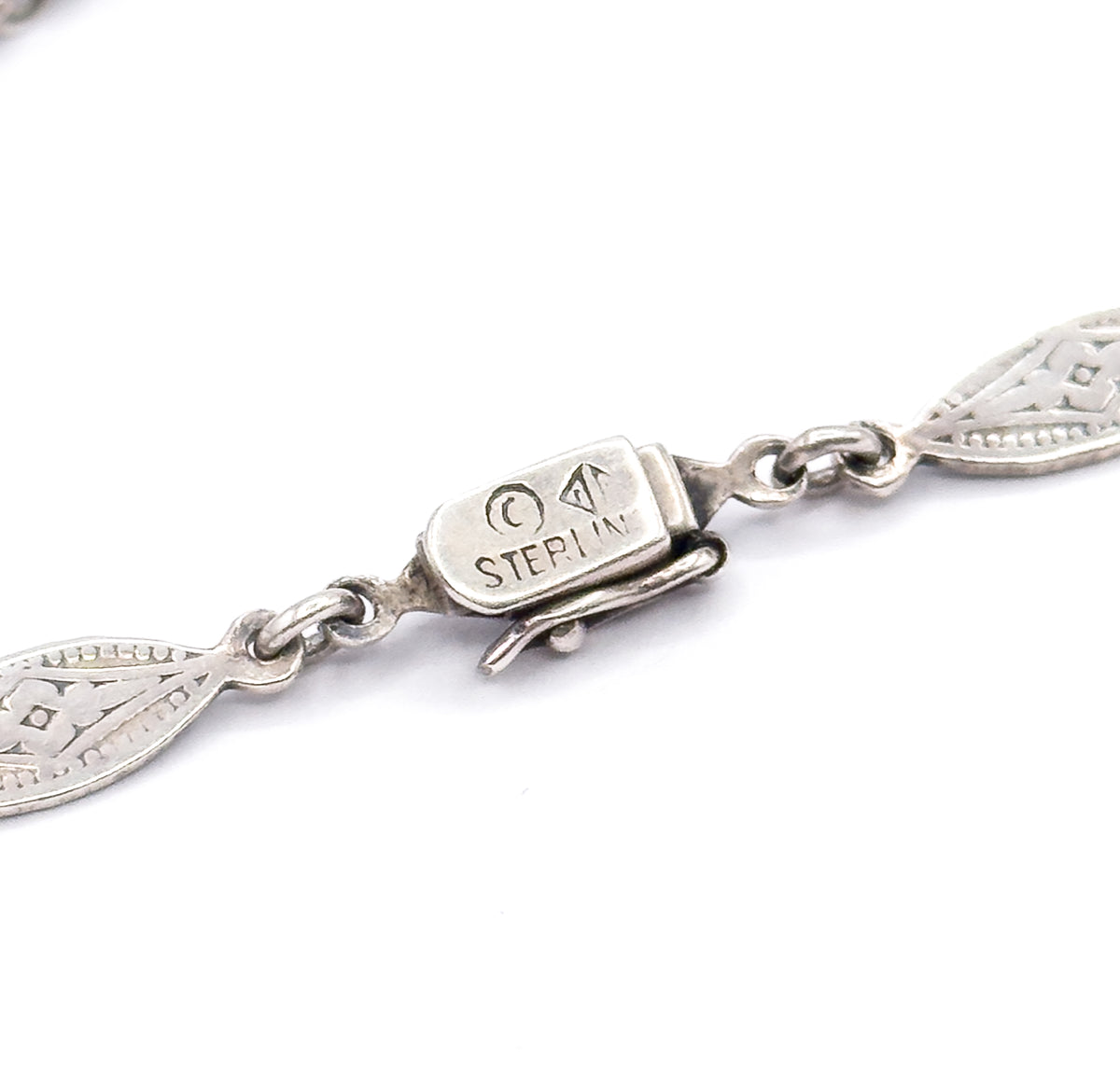Close view of the necklace's box clasp, stamped "Sterling" with a maker's mark and encircled letter, flanked by pierced pointed-oval links and the folded tongue of the catch.