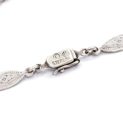 Close view of the necklace's box clasp, stamped "Sterling" with a maker's mark and encircled letter, flanked by pierced pointed-oval links and the folded tongue of the catch.
