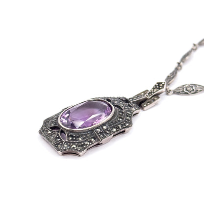 Low raking view across the pendant face, showing the scalloped marcasite-paved lower edge and the depth of the bezel, with one flower-patterned chain link visible at upper right.
